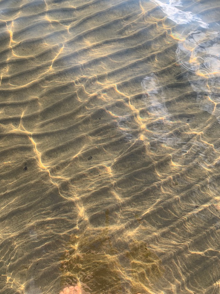 Ripples in sand with dappled sunlight at the surface of a lake