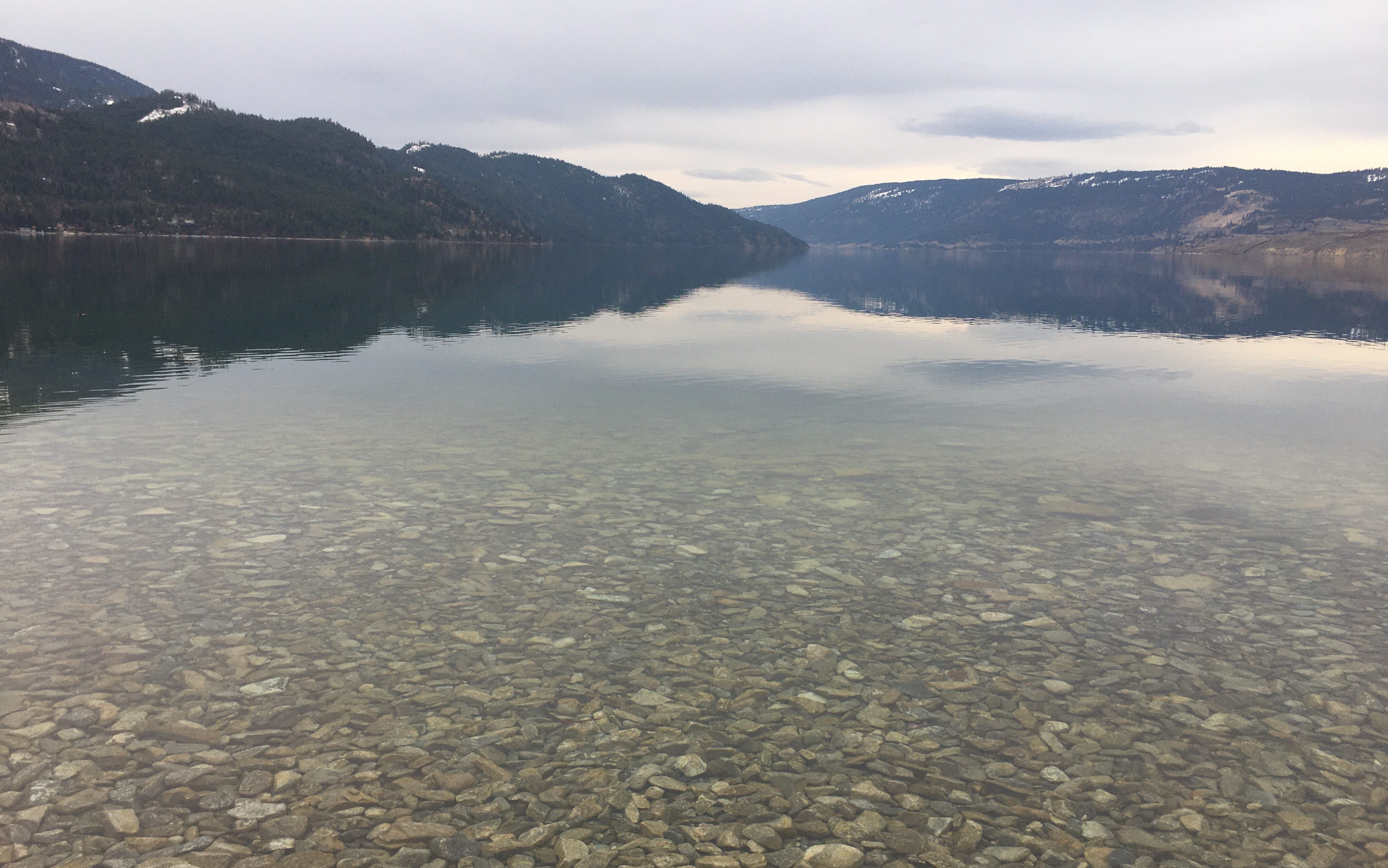Image of two dark brown hills overlapping at the end of a glassy lake