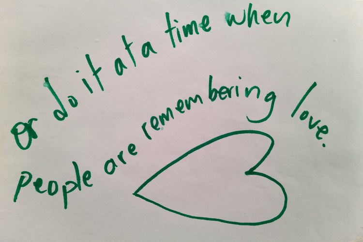 An index card on which the words "or do it at a time when people are remebering love" are written above a sideways sketch of a heart in green marker.