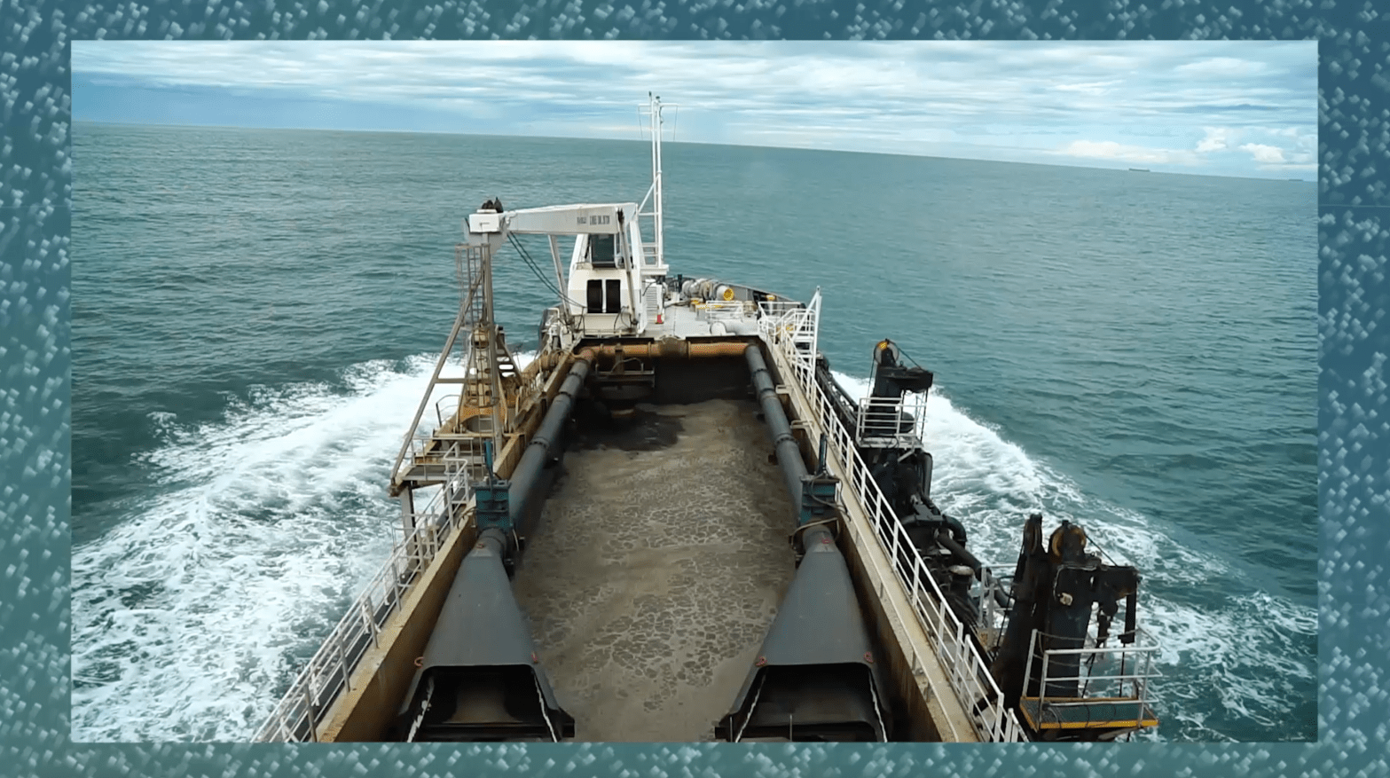 The bow of a ship moving through a blueish grey ocean. A tilted hoizon with a cloudy sky is in the background.