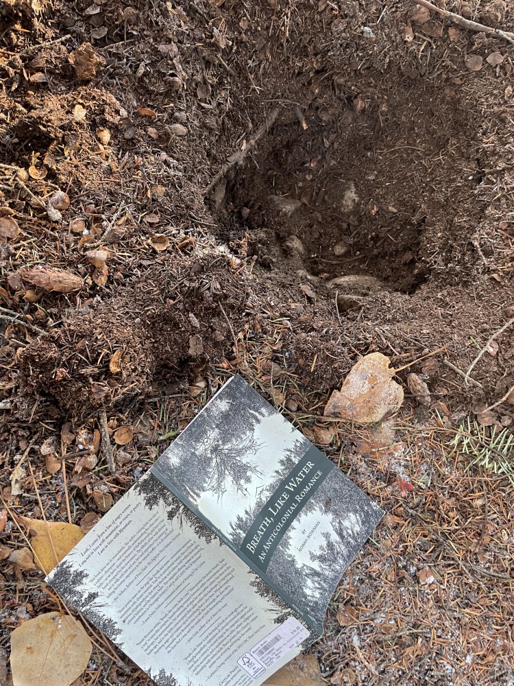 The book Breath, Like Water sits opened next to a hole in the ground.