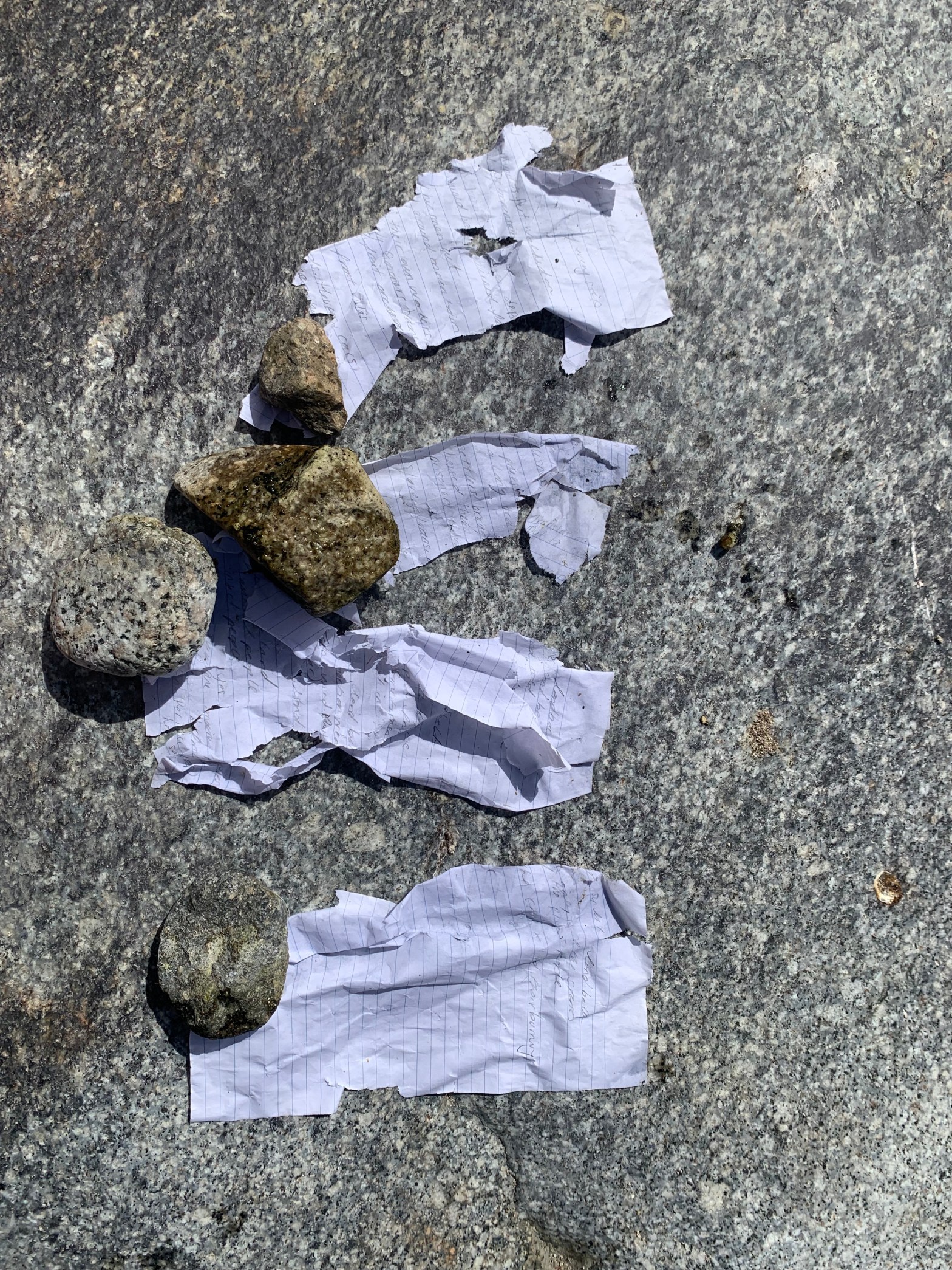 4 pieces of tattered paper are held in place by four grey stones of varying shapes and sizes.