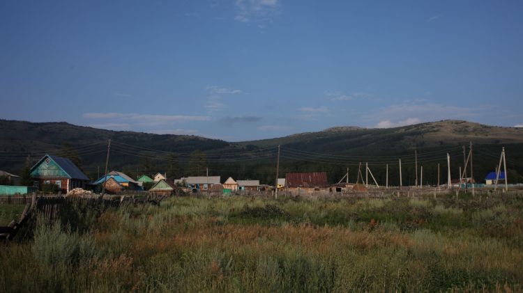 We are free, Olga F. Koroleva, 2013 / 2023 / A daytime image of the mountain range Irendyk at the height of summer. The colours are vivid, the skies blight blue, dark green forested mountains in mid image, and the foreground is a variety of greens and yellows of tall grasses.