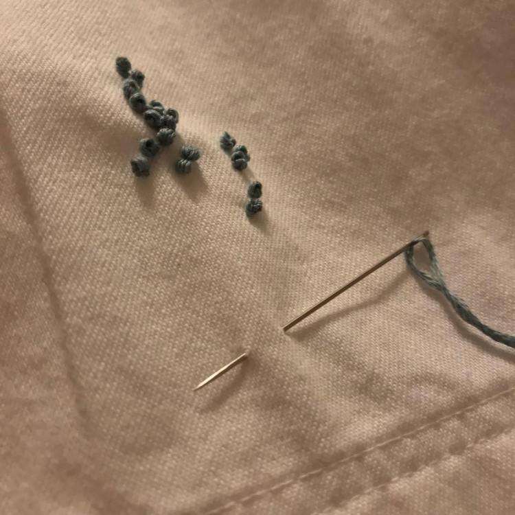 Wormwood triptych, left. Olga F. Koroleva, 2022-23 / A close up of dark green baubles of embroidered threads arranged to resemble wormwood inflorescence; the needle rests lightly pricked into the fabric.