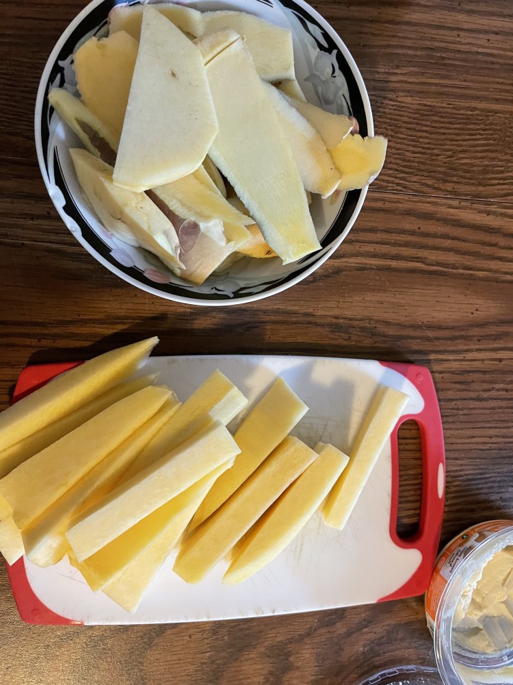 A cutting board with rutabega sticks. The discarded peelings of the outer rutabega are in a bowl beside.