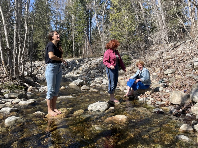 Three women dipping their feet into a shallow, rocky-creek on a fresh spring day