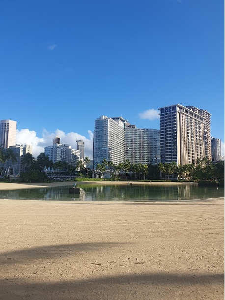 A sandy beach with a low pool of water with tall buildings