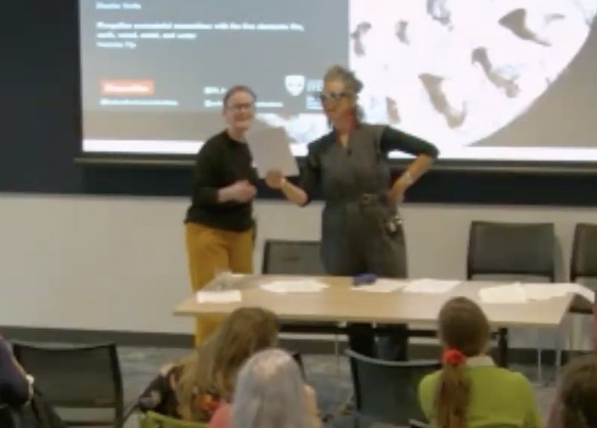 A blurry figure of two figures reading something in front of a crowd