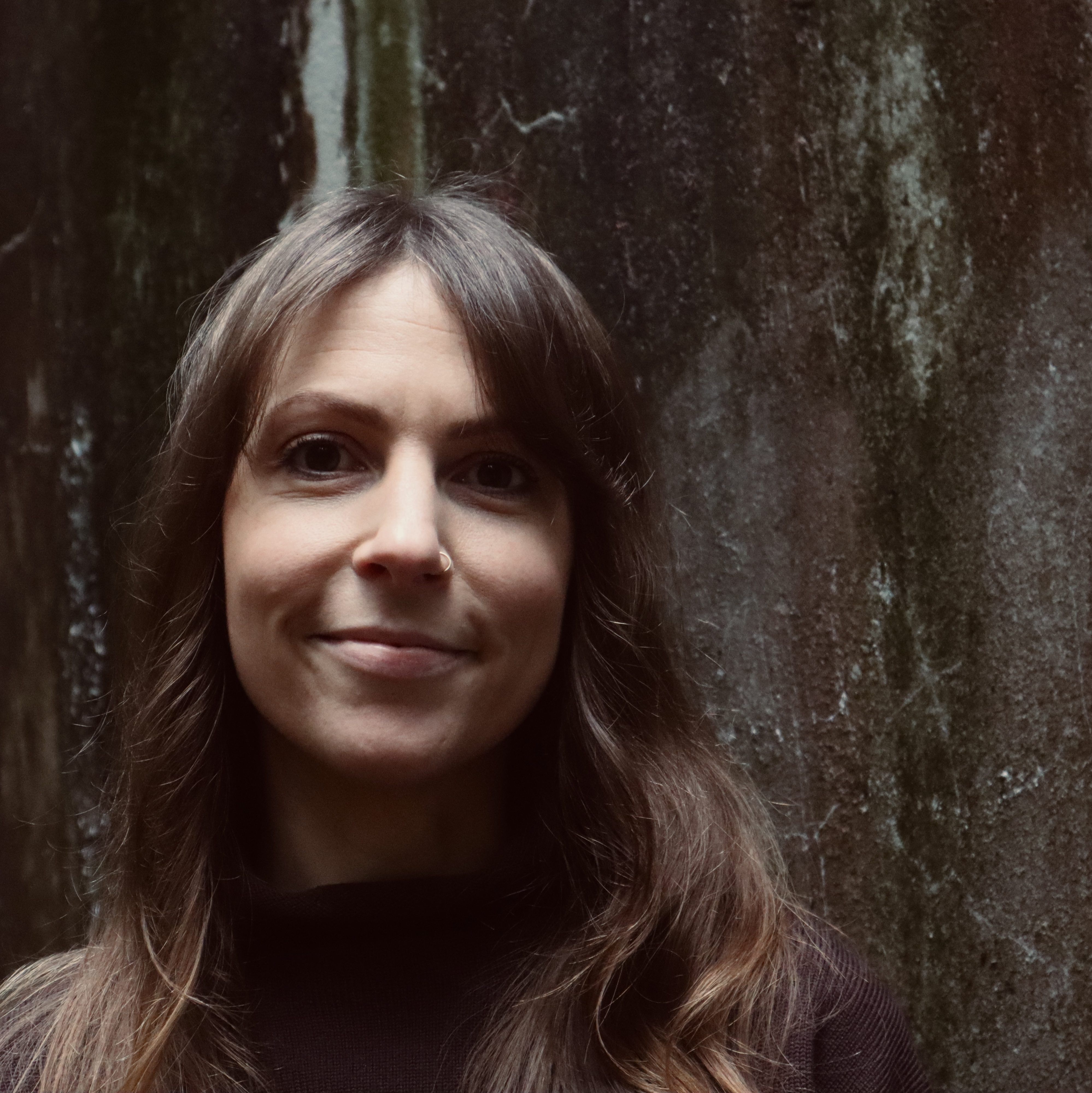 Headshot of a white cisgender woman in front of a rusted water tank