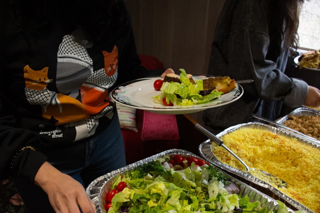 two people serving themselves Middle Eastern food from three different platters. The center of the picture is a person holding a plate with salad and bread.