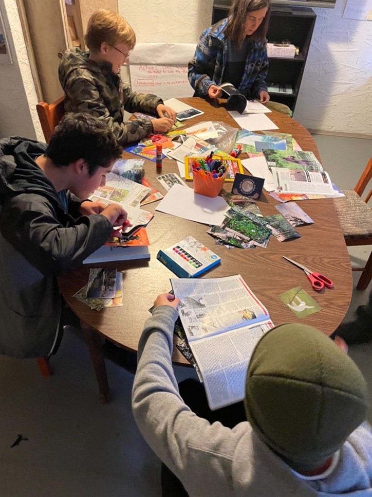 A group of students sitting around a table full of crafting material, they are making collages.