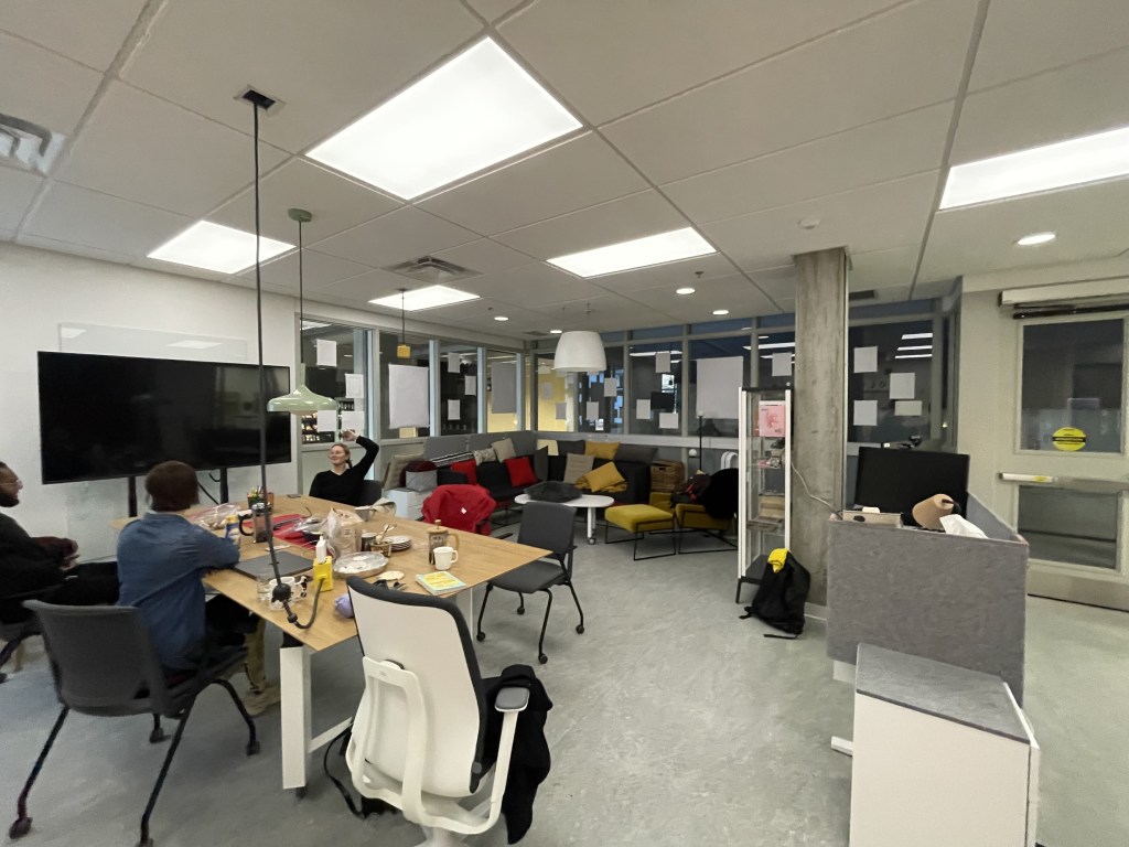 A wide shot of the Lab space, including a couch with cushions, a table covered with snacks and mugs, a desk with soft edges.