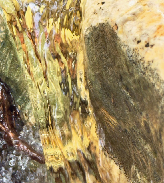 A column of water, held in a moment as it falls between rocks; it refracts roots sipping at the river and the amber, burnt umber and yellow of the rocks. 