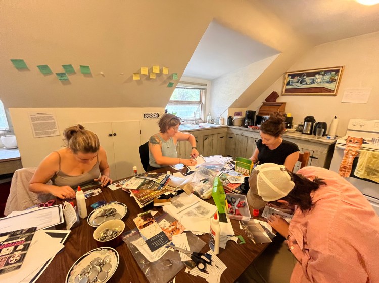 4 individuals sit around a table with a mess of craft supplies in front of them