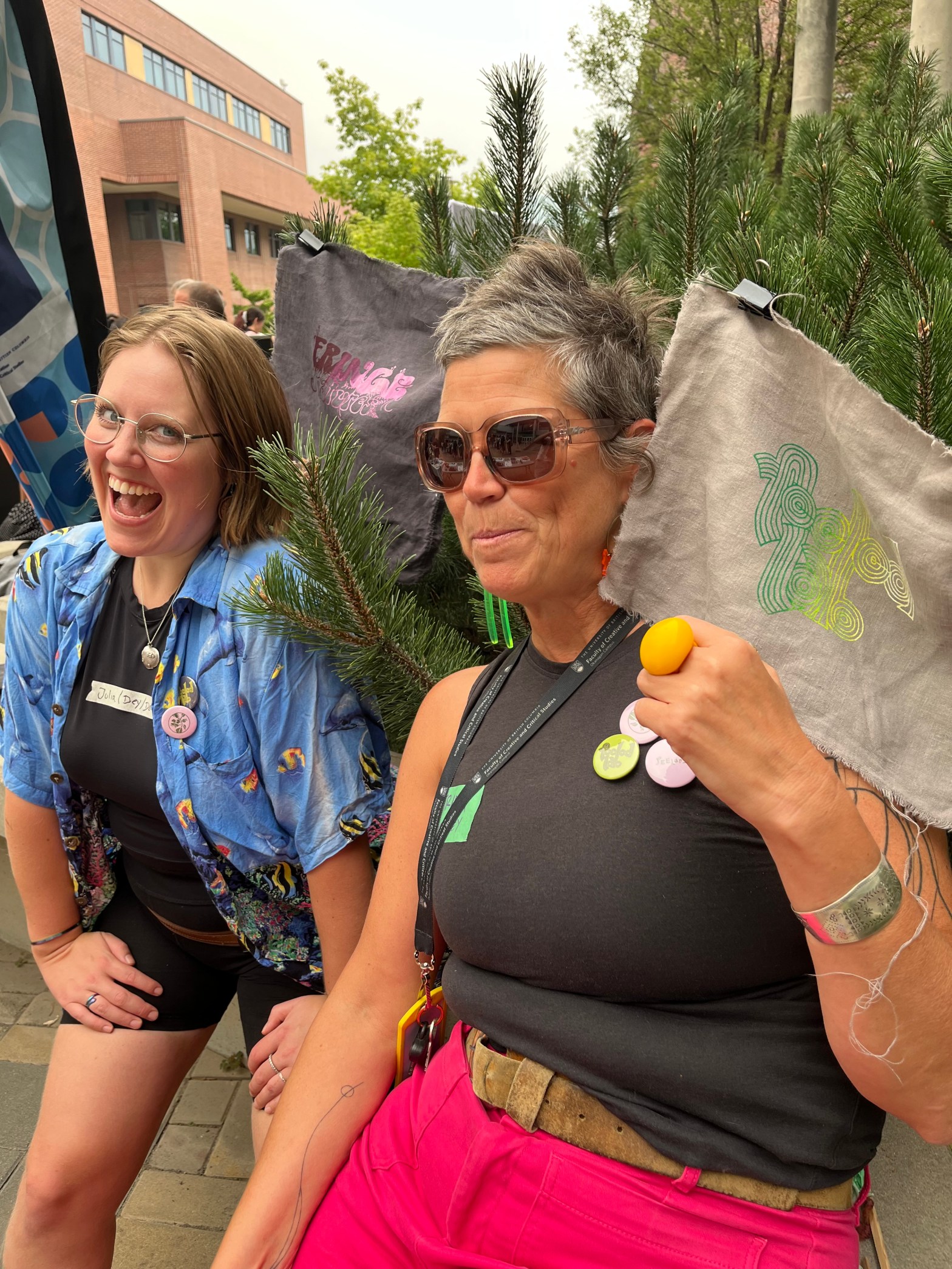 Julia and Astrida in front of a Ponderosa Pine with FEELed Lab buttons and patches in the background