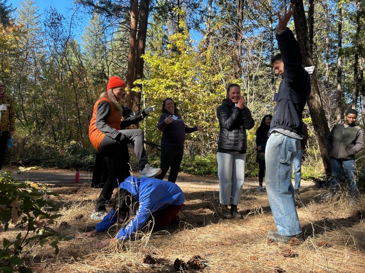 People enacting a story in the forest. One person is crouching on the ground, another is stretching high up into the sky.