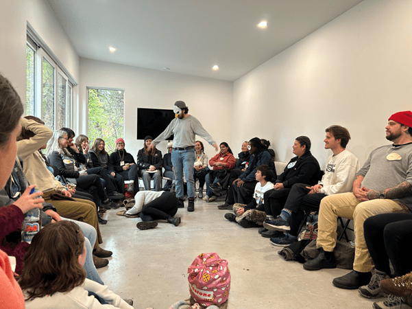 A group of people sitting in a circle in Woodhaven Studio. Two people are enacting a syilx creation story featuring eagle, coyote and fox.