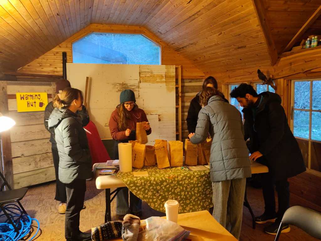 A group of people standing around a table with brown paper bags containing wildflower seeds