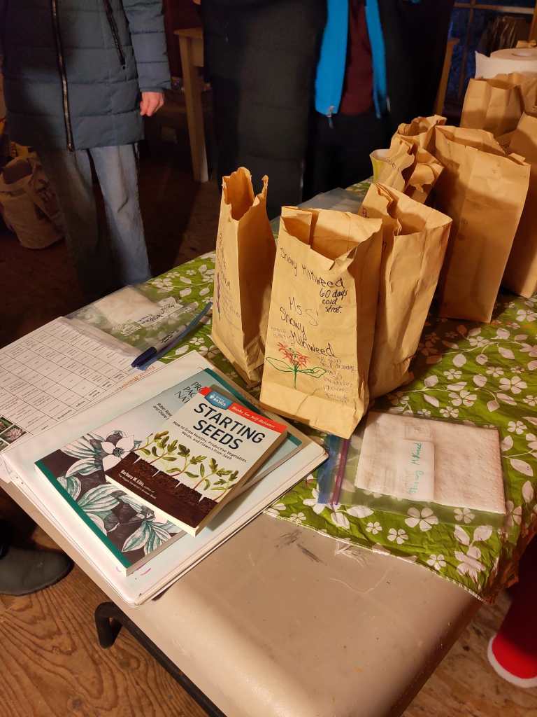 A bunch of native seed planting books and brown paper bags with seeds on a table