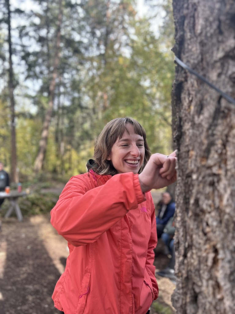 Erin is laughing and carefully touching the bark of a large tree.
