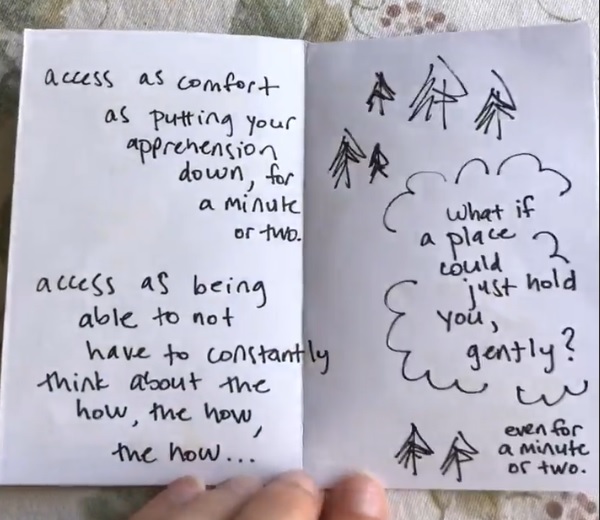 A two-page zine spread is held against a tablecloth with green leaves. The pages are white with black ink text and a few drawings. The first page has a poem reading “access as comfort, as putting your apprehension, down for, a minute, or two. access as being, able to not, have to constantly, think about the, how the how, the how …”. The second page has trees with a bubble containing text, “What if a place could just hold you, gently? even for a minute or two.”