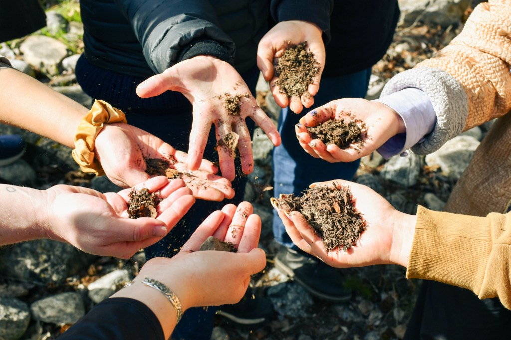 close up of seven hands holding a handful of dirt in a circle