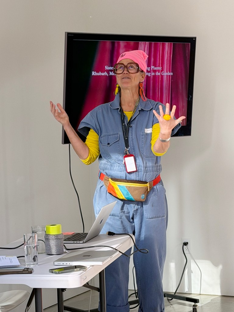 Astrida introducing Cate wearing a jumpsuit and holding her hands up to the sky