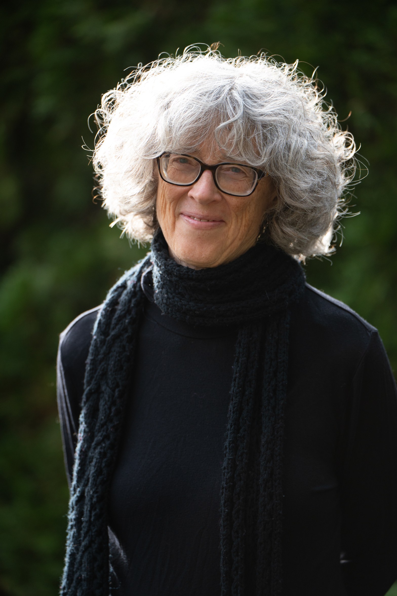 Headshot of Nancy Holmes wearing a black sweater in front of a blurry forest.