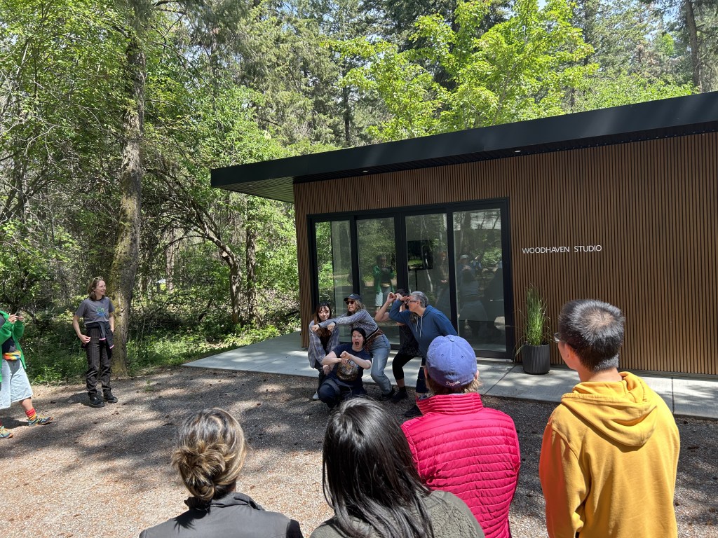 A small group of people making a tableau of their experience in front of Woodhaven studio, witnessed by the rest of the group.