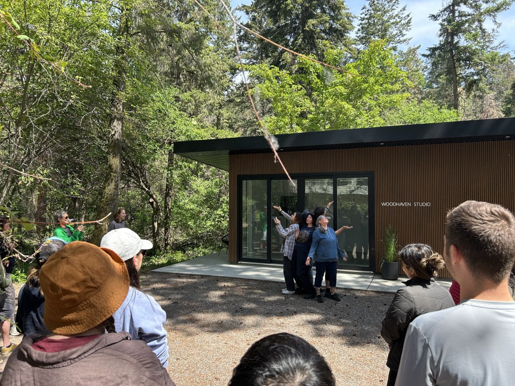 Another tableau of a small group of people, they are standing upright with their backs to each other looking up towards the trees.
