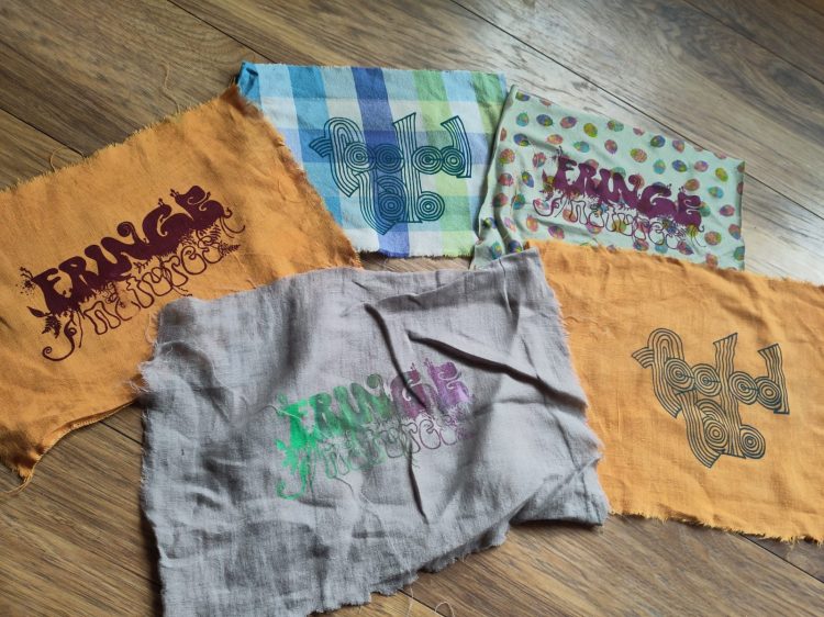 FEELed Lab fabric patches in orange, gray and different patterns spread out on the floor. Some patches have a "Fringe Natures" print, others show the FEELed Lab logo.