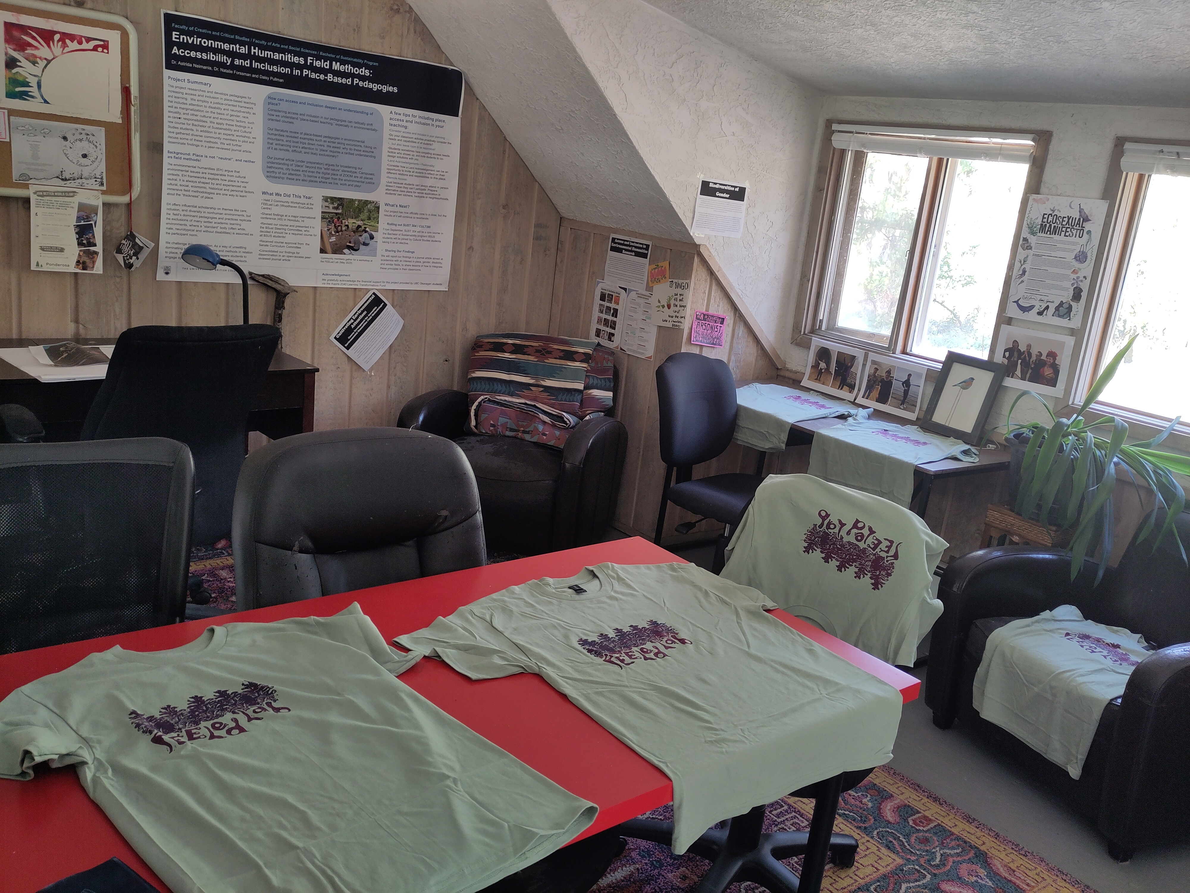 Desks in the FEELed Lab with newly printed light green t-shirts with the new FEELed Lab logo printed in dark red and blue. It shows five pine cones with the words "FEELed Lab"