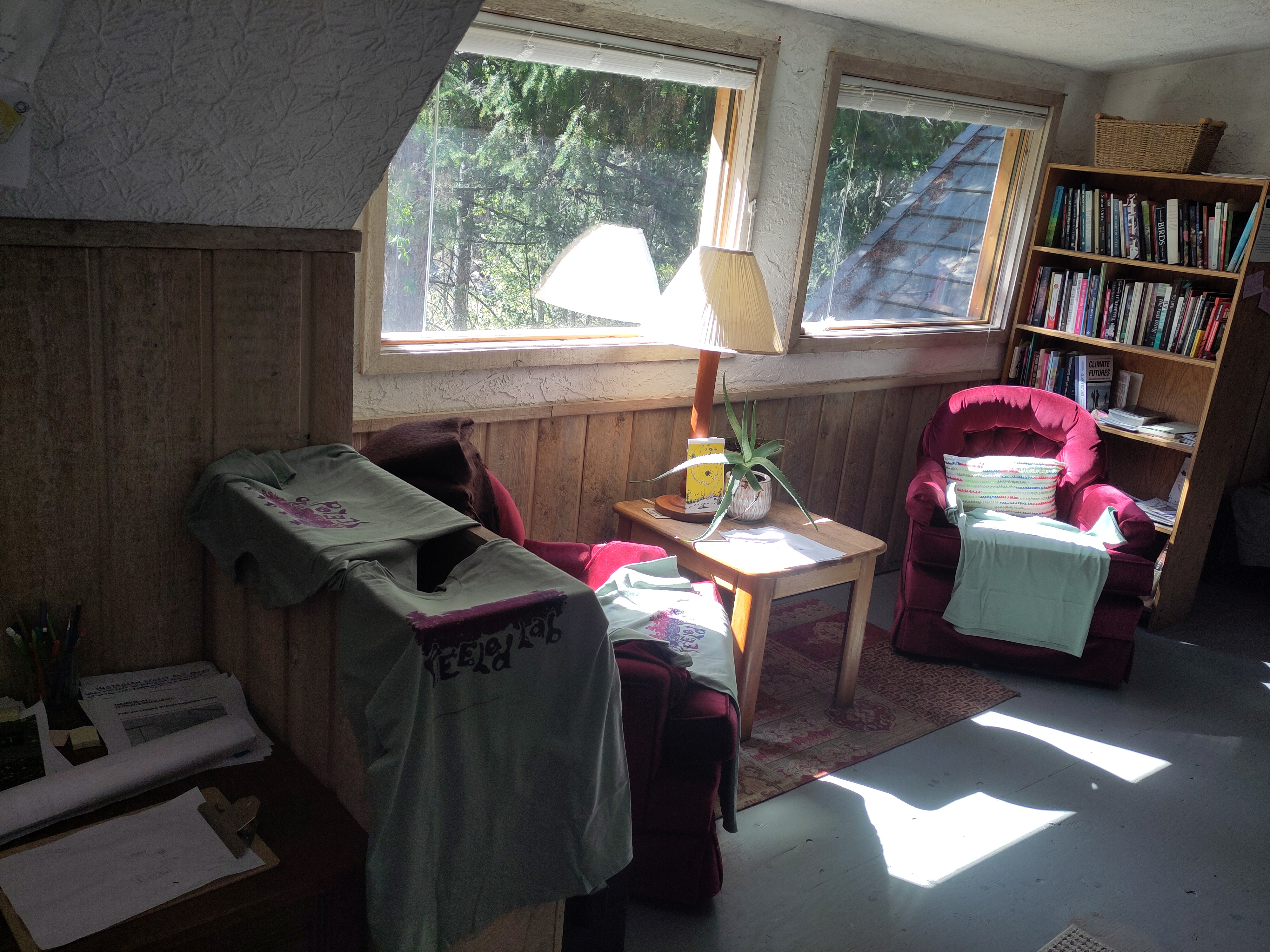 The FEELed Lab library (two red velvet chairs next to a little table with a lamp underneath a window in front of a bookshelf). Newly printed shirts are draped over the chairs