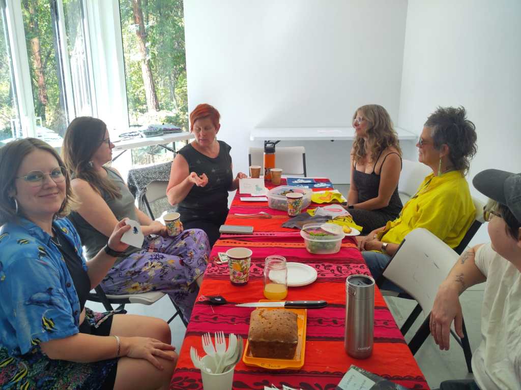 FEELed Lab friends and members sitting around a table with a red tablecloth sharing crafts and talking.
