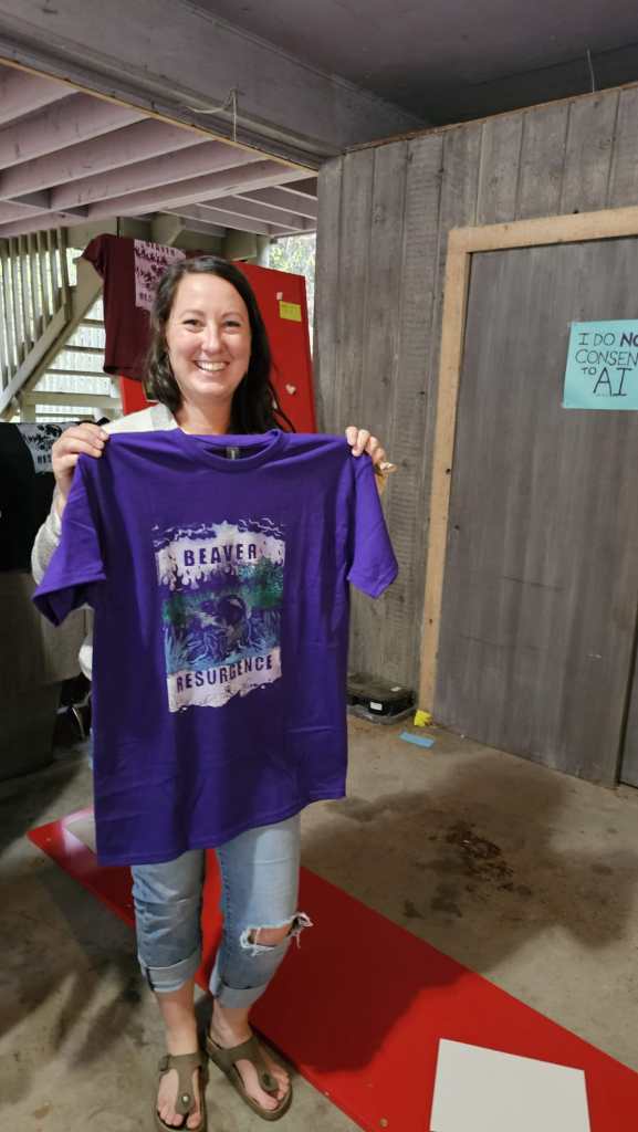 Someone holding up a freshly printer purple "Beaver Resurgence" shirt